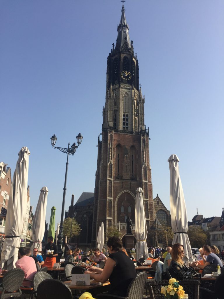 Old church in Delft with people sitting in cafes in the square