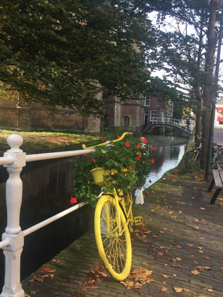 Yellow painted bicycle leaning against the railing of a Delft canal